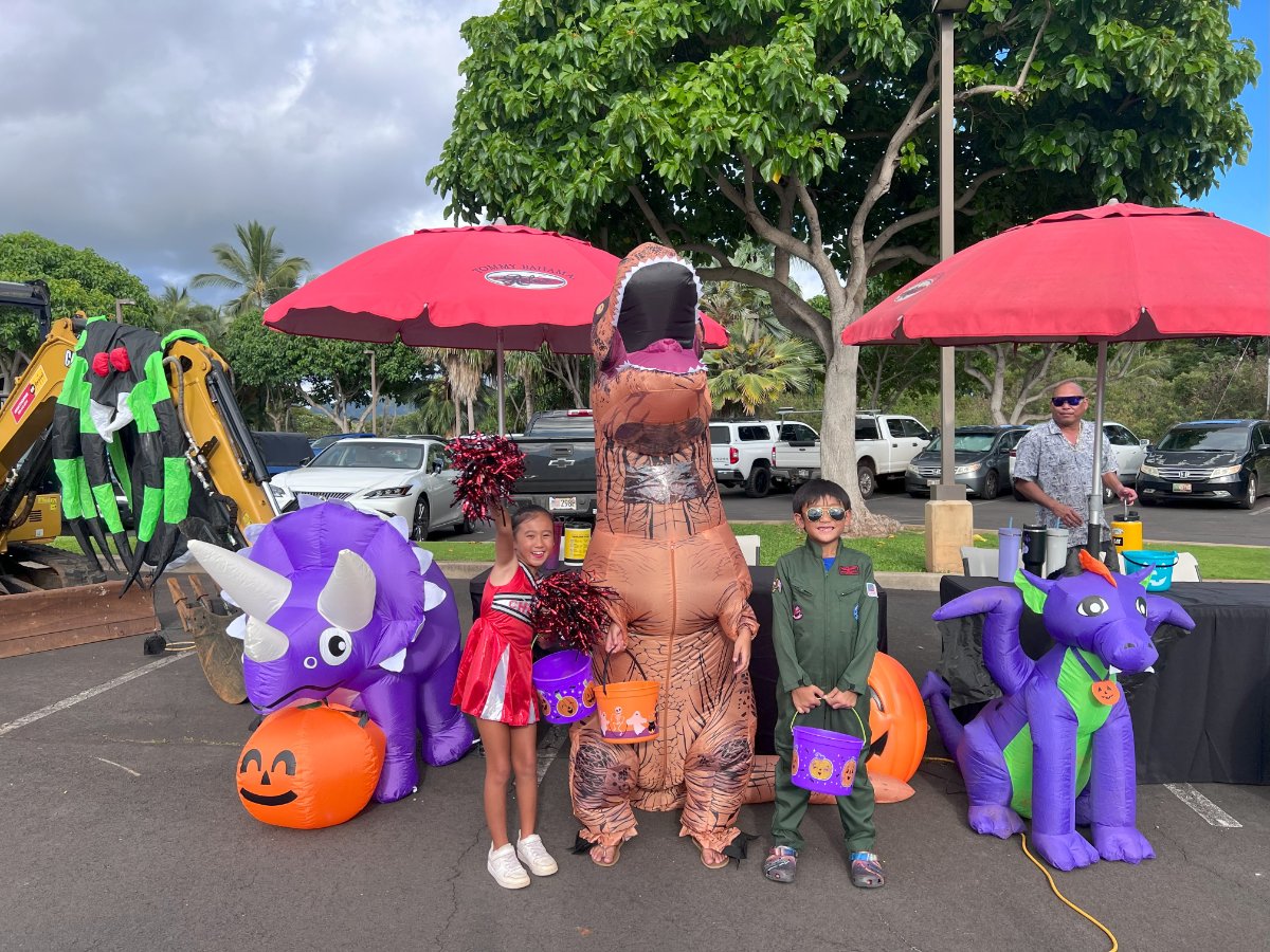 Kids in costumes with trick-or-treat buckets beside Halloween inflatables